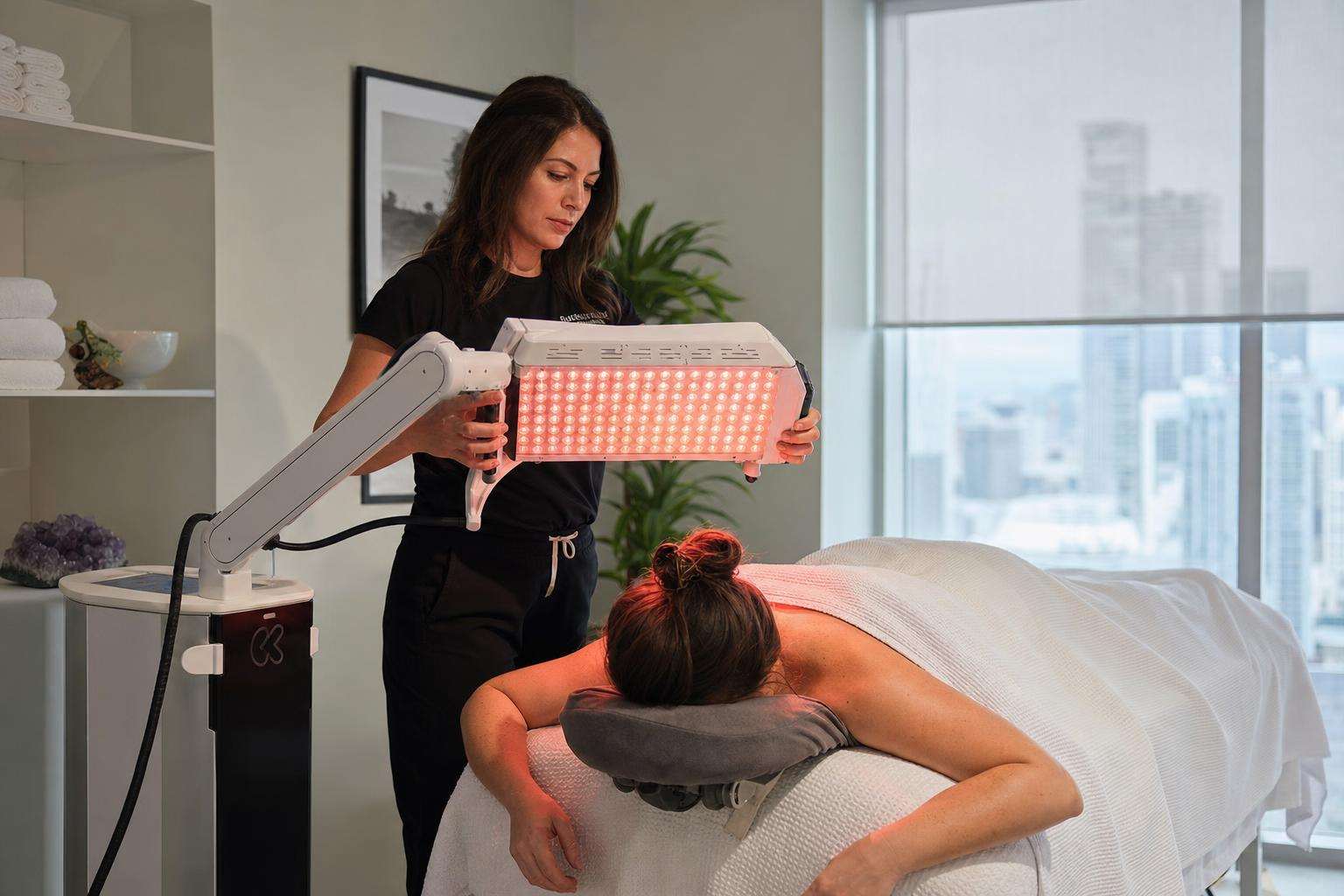 Red and near-infrared LED therapy panel glow in a clean clinical-style room, no people