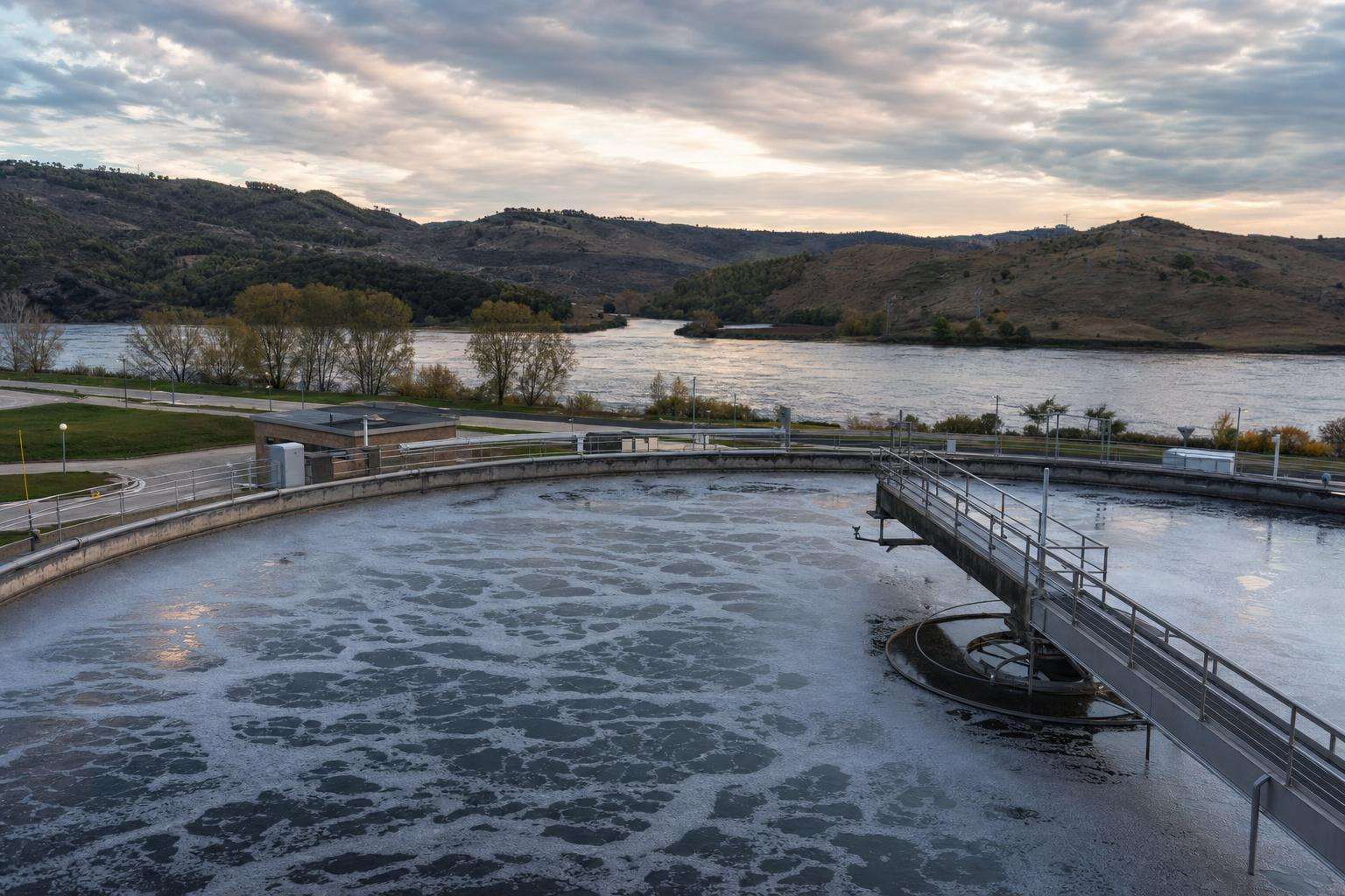 Wastewater treatment plant aeration tanks under open sky with a clean river visible downstream
