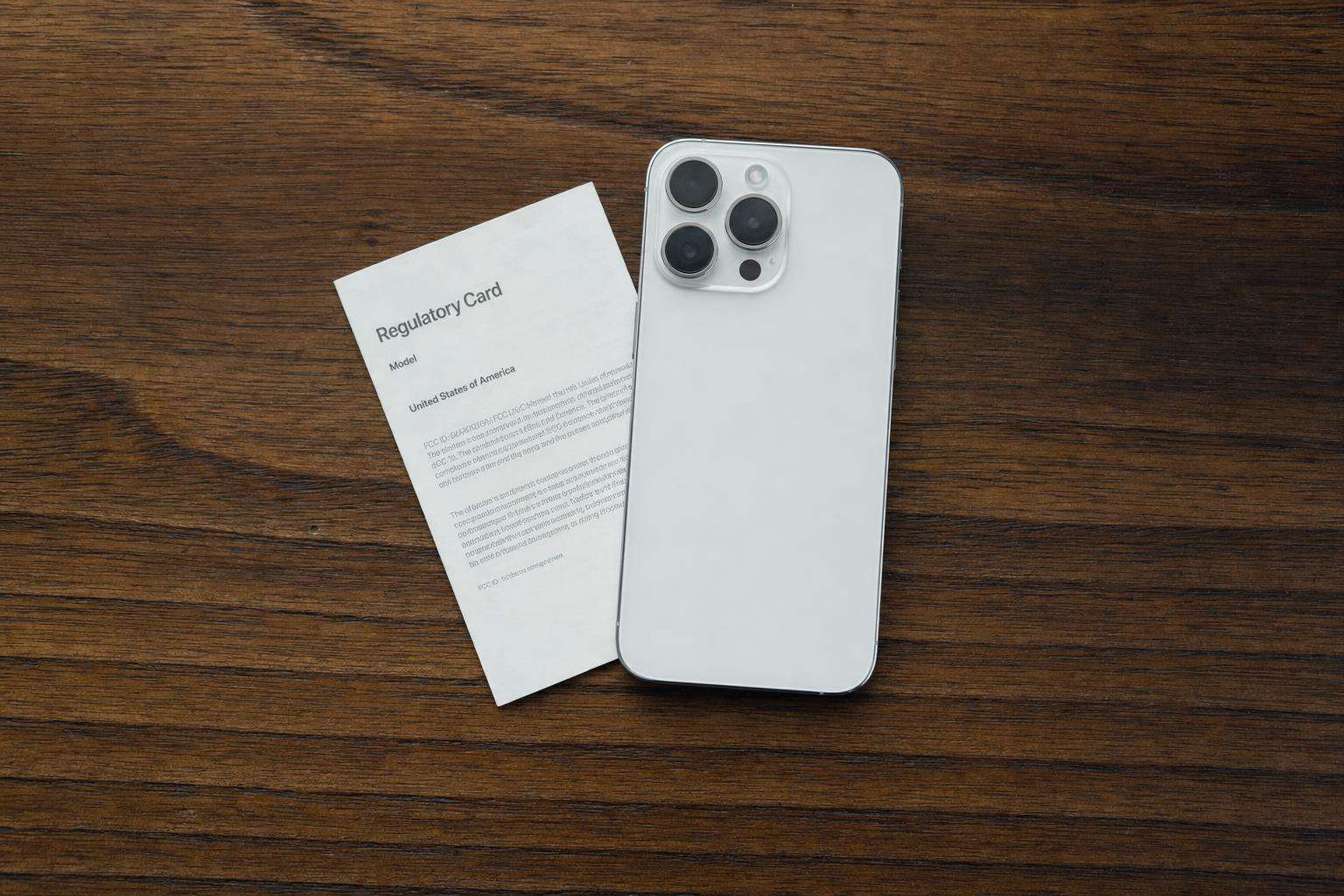 Smartphone face-down next to FCC regulatory label card, soft desk light, no people