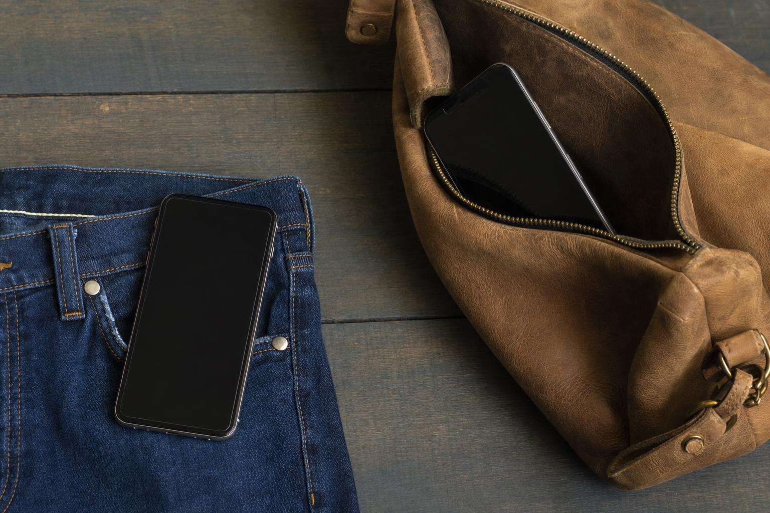 Two phones on desk—one near keys, one near bag—soft office light, no people