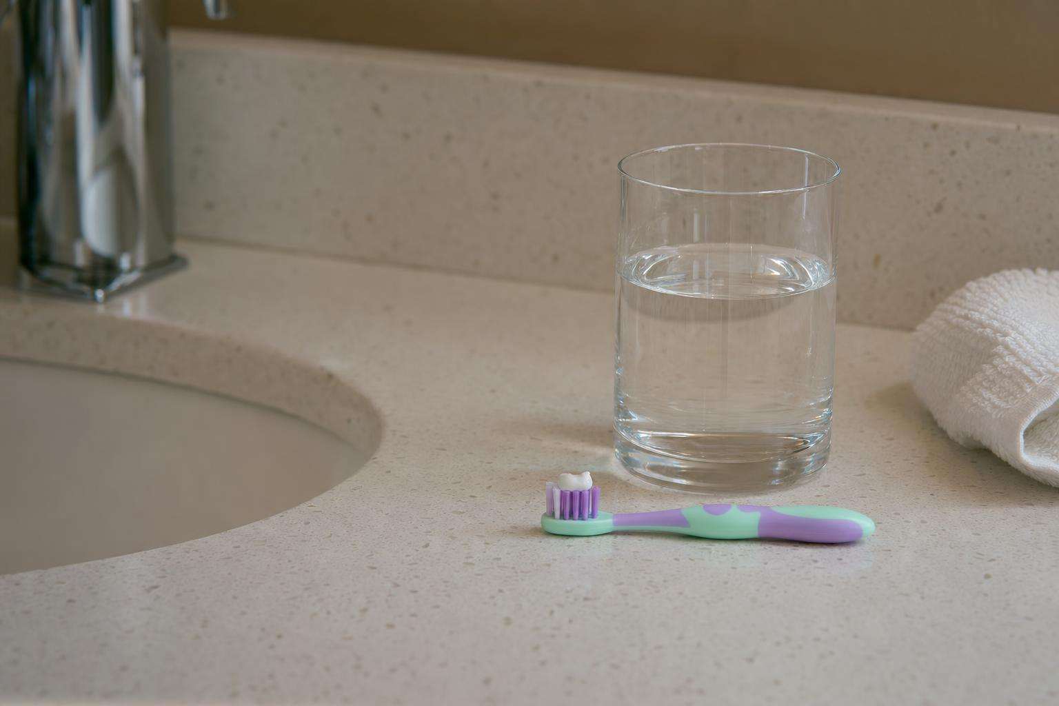 Child-sized toothbrush with pea-sized toothpaste next to a glass of tap water on a bathroom counter